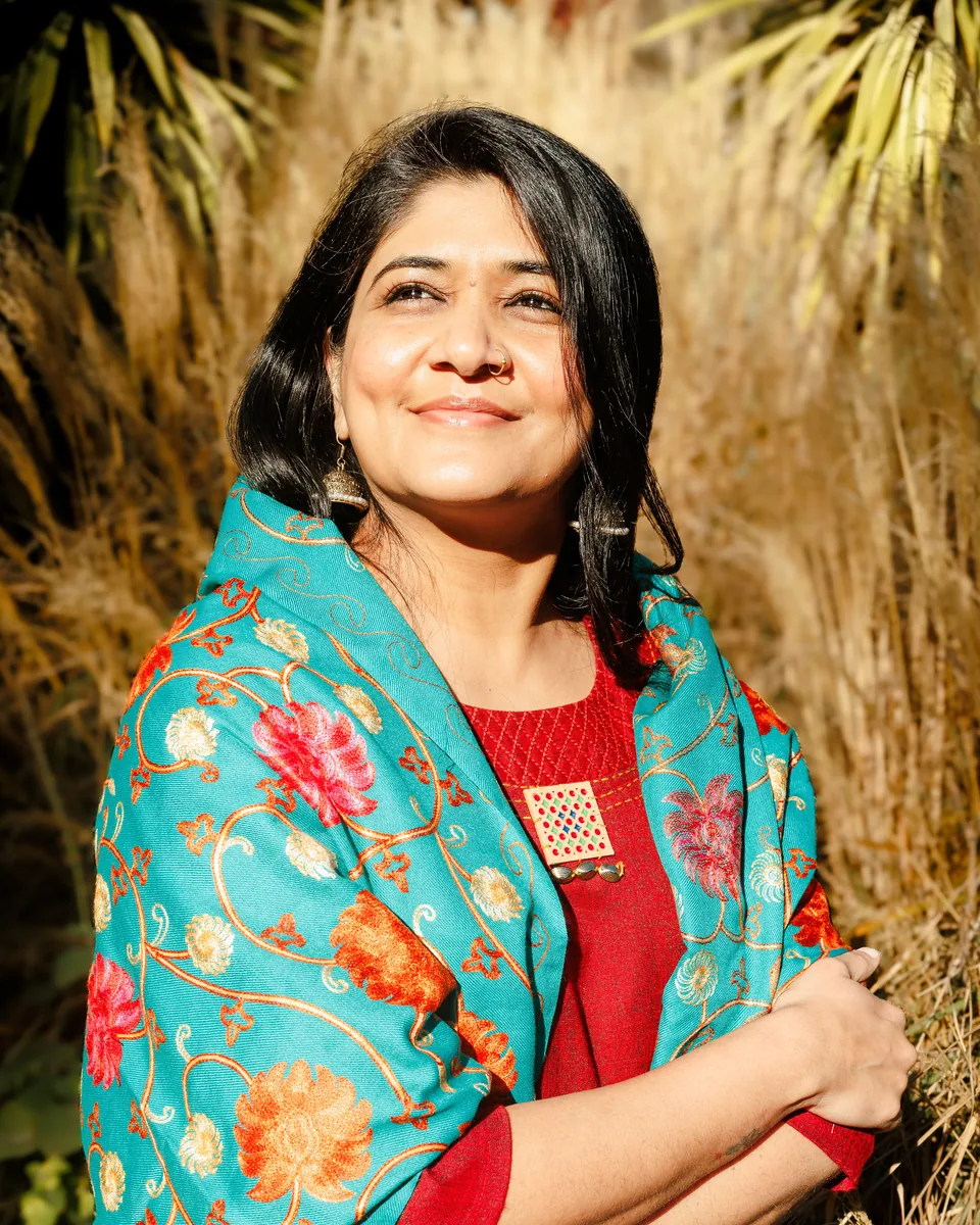 Harsiddhi Pancholi in a teal floral shawl, smiling and looking up into the sunlight